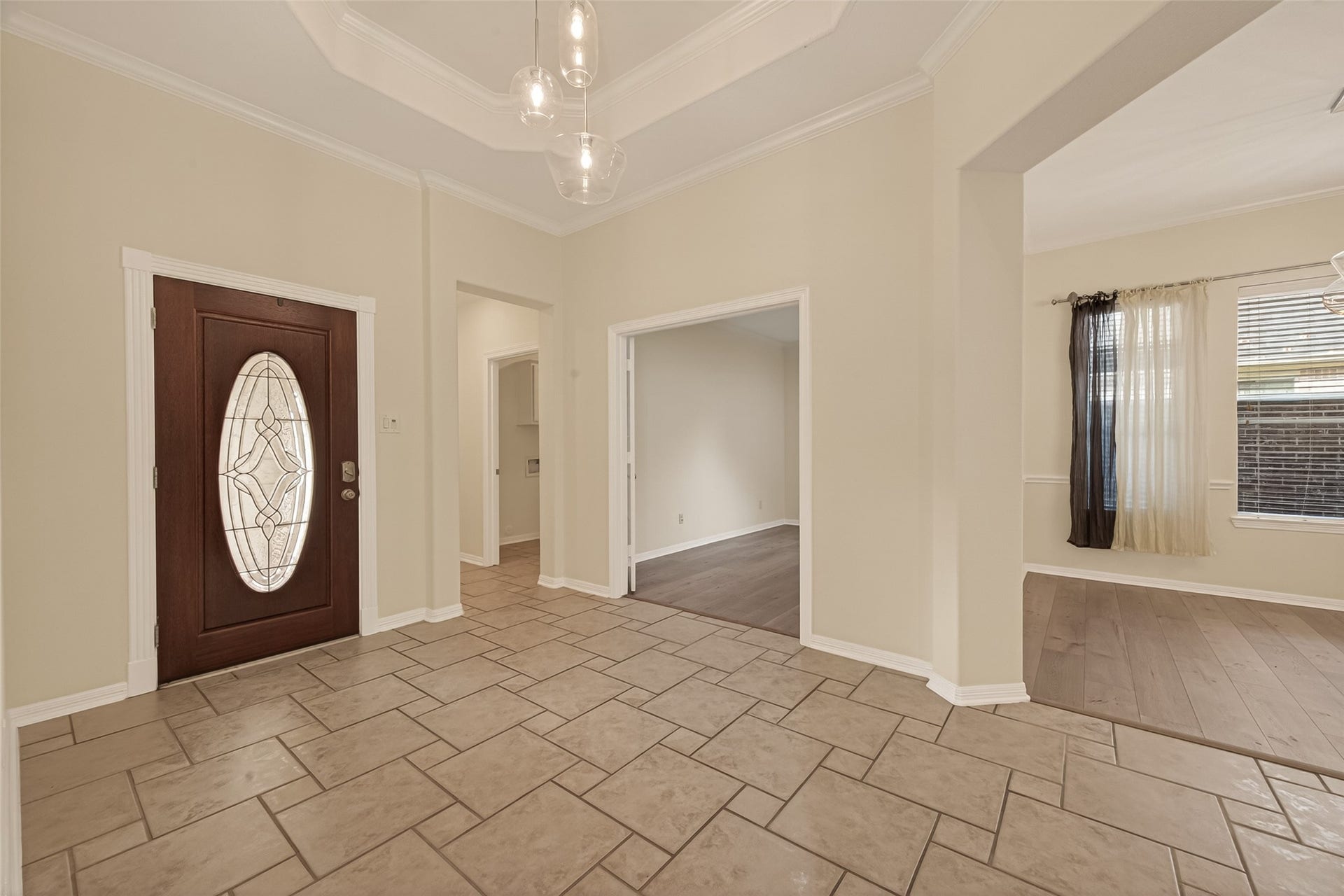 10106 Lost Hollow Lane, Missouri City, TX 77459 This welcoming entryway features a stylish front door with decorative glass, elegant tile flooring, and neutral walls. The space connects to a room with wood flooring and large windows, providing a bright, open feel.