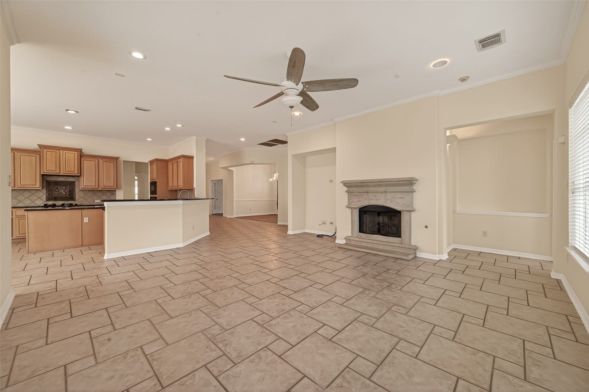 10106 Lost Hollow Lane, Missouri City, TX 77459 This spacious open-concept living area features tile flooring, a ceiling fan, and a stone fireplace. The room seamlessly connects to a modern kitchen with wooden cabinetry and a breakfast bar, offering ample natural light and a welcoming atmosphere.