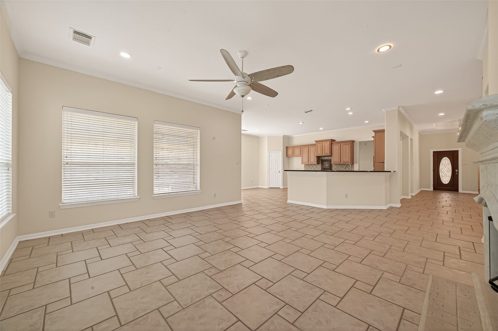 10106 Lost Hollow Lane, Missouri City, TX 77459 This spacious open-plan living area features large windows for natural light, a ceiling fan, and tiled flooring throughout. The kitchen has ample cabinetry and a breakfast bar, flowing seamlessly into the living space, ideal for entertaining.