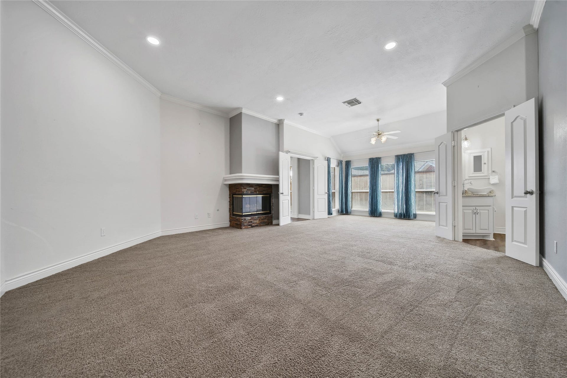 5918 Greenway Manor Lane, Spring, TX 77373 Spacious primary bedroom filled with natural light, high ceilings, a cozy stone-accented fireplace, and ample room for a sitting area. Double doors lead to the en-suite bathroom, completing this inviting retreat.