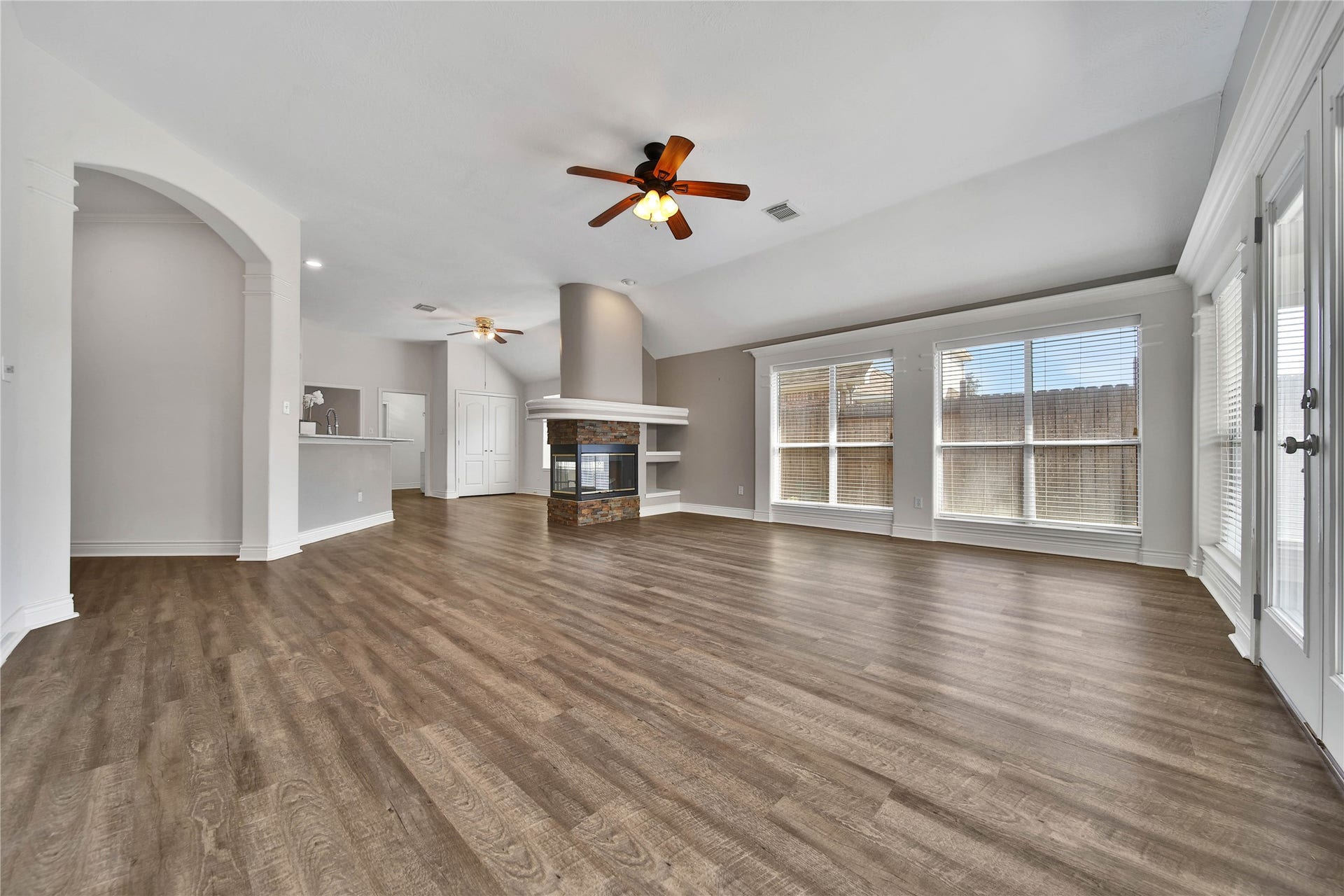 5918 Greenway Manor Lane, Spring, TX 77373 Light-filled living area with large windows and an accented fireplace with built-in shelving, connecting the kitchen and breakfast area in this open layout concept, creating an inviting space for everyday living and entertaining.