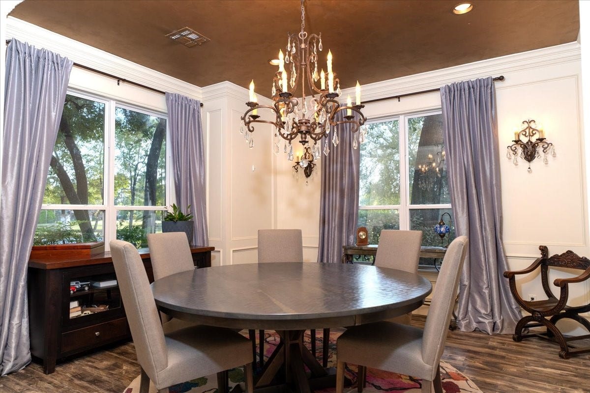 8514 Haven Way, Tomball, TX 77375 Formal dining room made for holiday dinners and special occasions, with a crystal chandelier, and decorative wall molding. Large windows frame views of the mature trees outside.