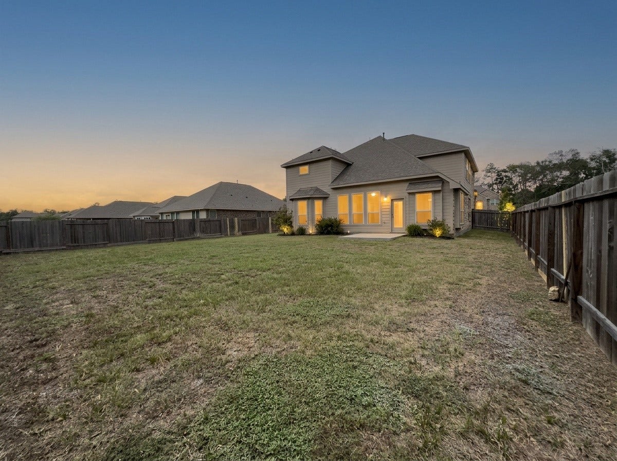 662 W Linnwood Drive, Woodbranch, TX 77357 Spacious fenced backyard with a well-lit two-story home, perfect for outdoor activities and entertaining.