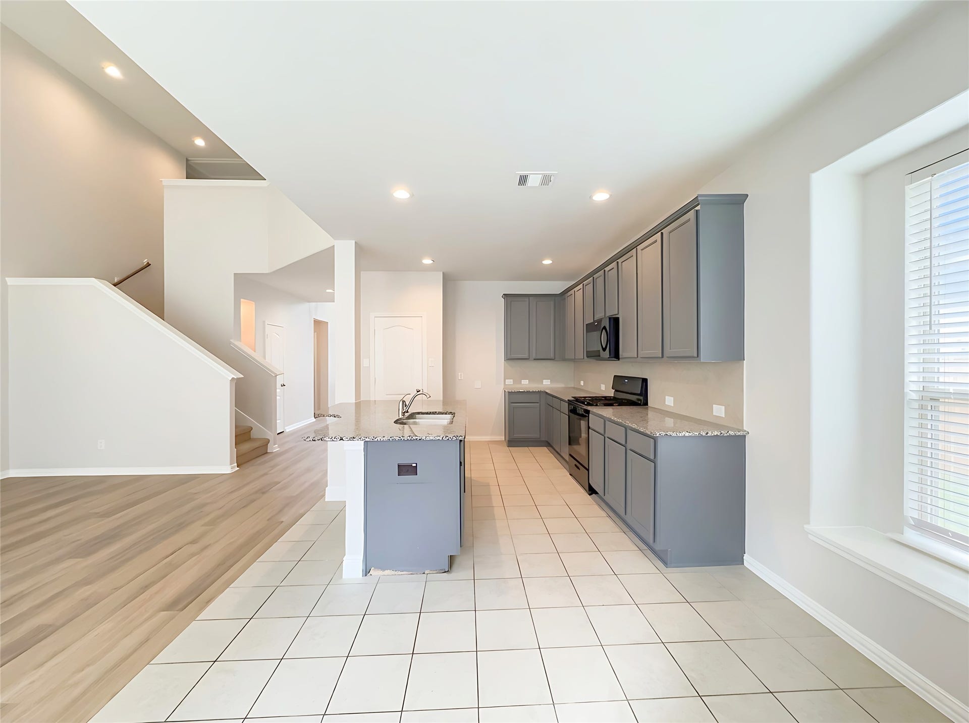 662 W Linnwood Drive, Woodbranch, TX 77357 Spacious open-concept kitchen with modern gray cabinetry, granite countertops, and a large island, seamlessly connecting to the living area with hardwood flooring and a staircase leading to the upper level.