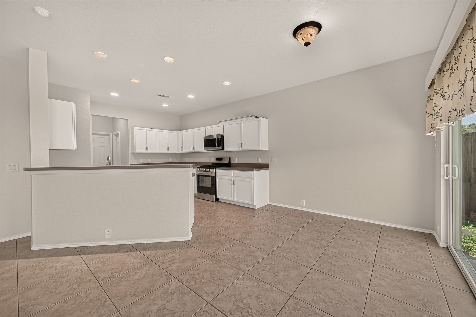 26130 Ripley Hills Drive, Richmond, TX 77406 This spacious kitchen features modern appliances, ample white cabinetry, and a large countertop area. The open layout connects to a tiled dining area with plenty of natural light from sliding glass doors.