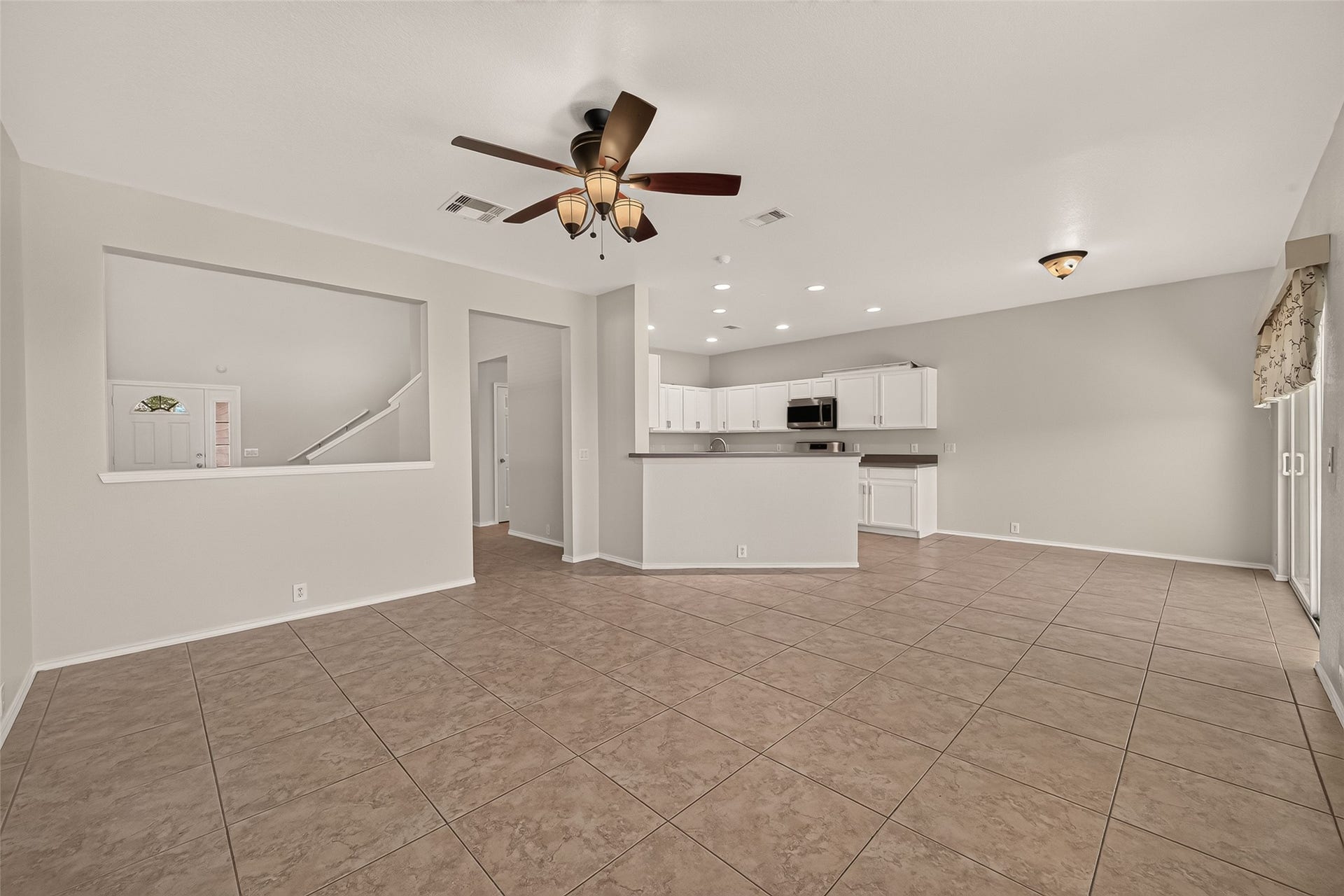 26130 Ripley Hills Drive, Richmond, TX 77406 This spacious open-concept living area features a tiled floor, ceiling fan, and ample natural light. It seamlessly connects to a modern kitchen with white cabinetry and a breakfast bar, perfect for entertaining.