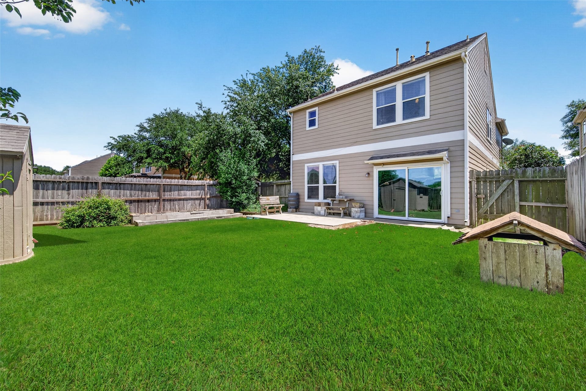 26130 Ripley Hills Drive, Richmond, TX 77406 This backyard features a spacious, grassy area with a wooden fence for privacy. There's a concrete patio with seating, perfect for outdoor relaxation or entertaining. The exterior of the house is a modern two-story design with large windows that offer plenty of natural light.