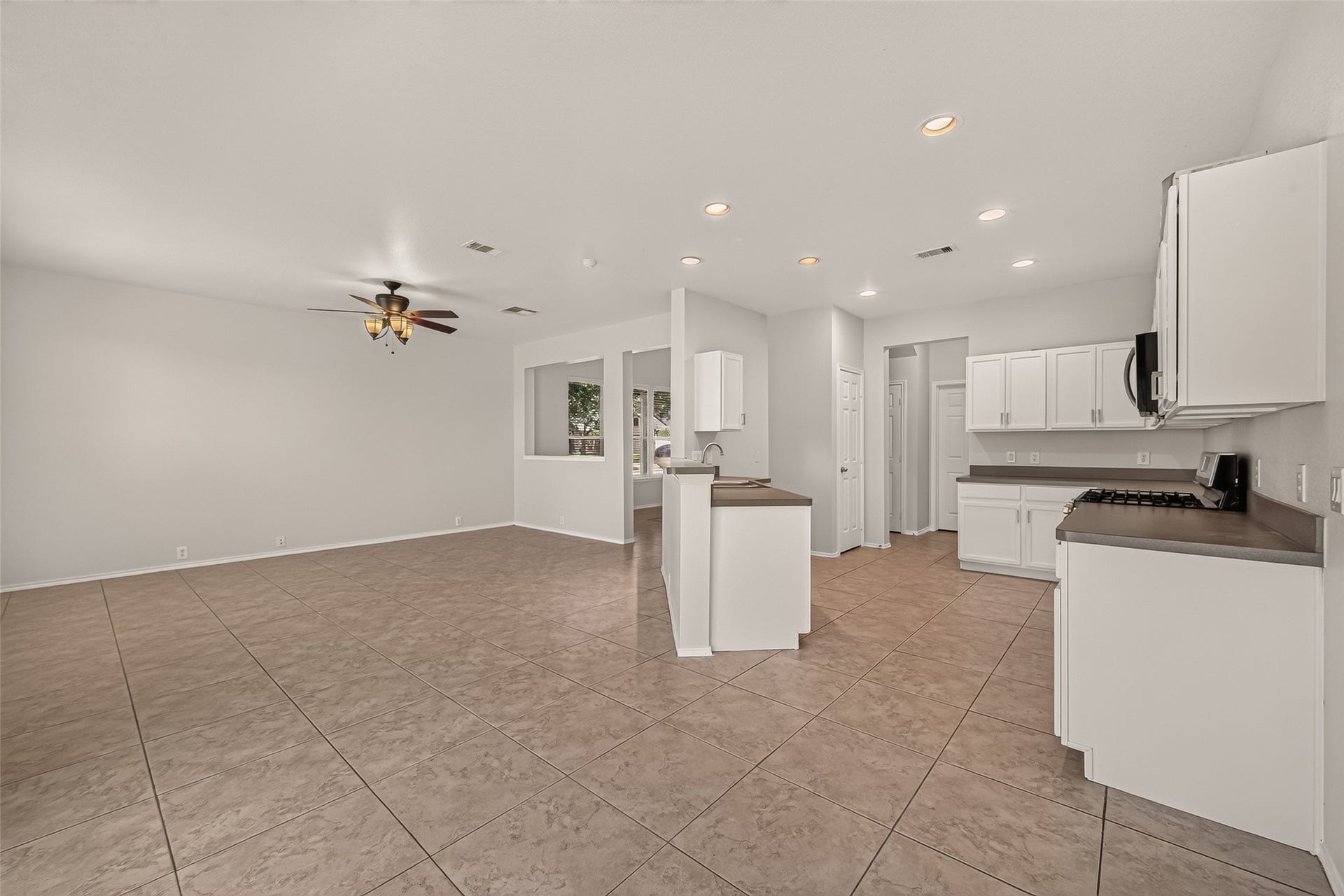 26130 Ripley Hills Drive, Richmond, TX 77406 This photo showcases a spacious open-concept living area with tiled floors, a modern kitchen featuring white cabinetry, and a ceiling fan. The area is well-lit with recessed lighting and offers ample space for versatile furniture arrangements.
