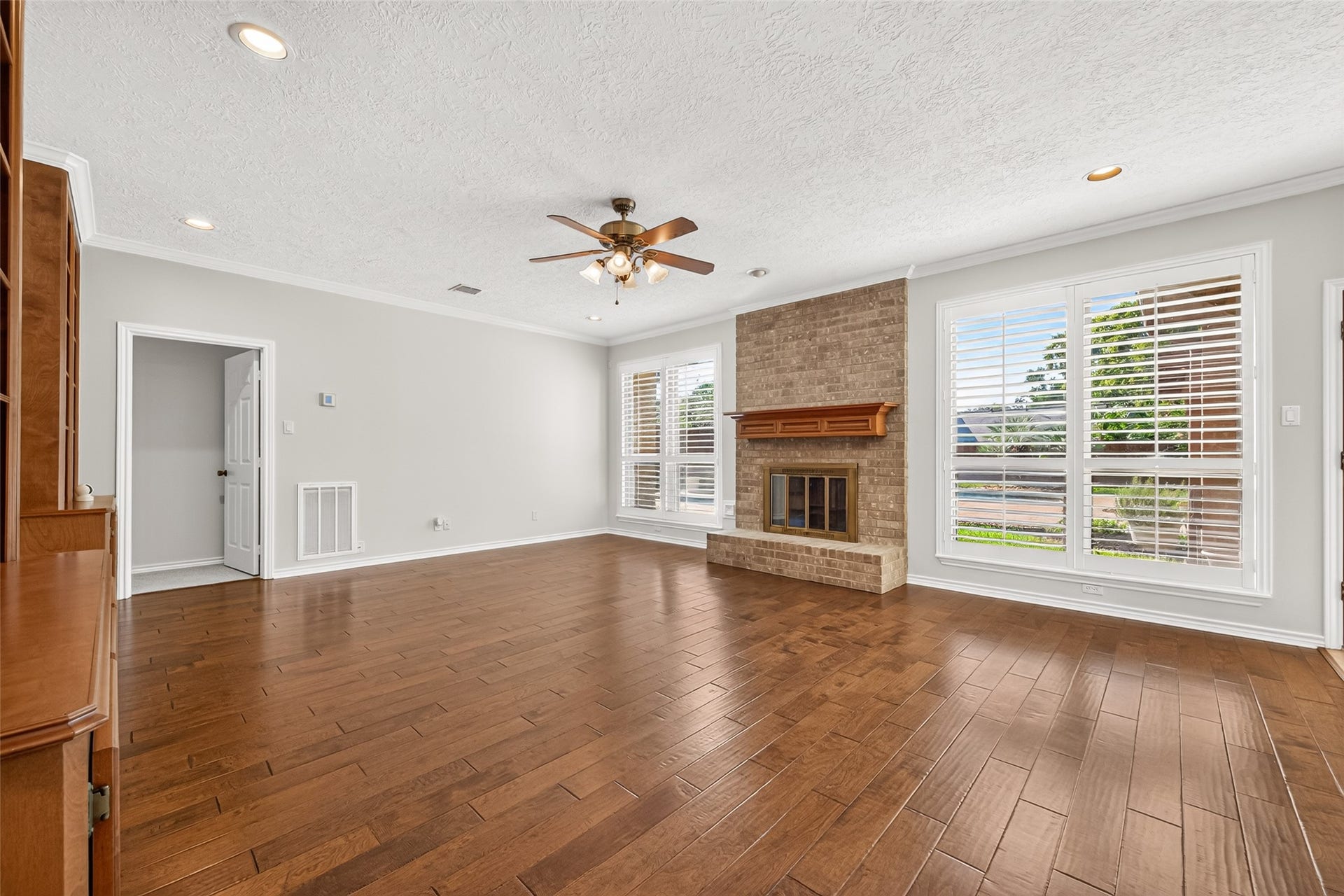 WARM & INVITING WITH A VIEW! The impressive floor-to-ceiling brick fireplace features a handsome wood mantel & glass-and-brass doors, creating a beautiful focal point for this comfortable living space. A wall of windows with plantation shutters overlooks the backyard swimming pool, offering a lovely view of the outdoor retreat as well as a way to keep an eye on kids playing outside. A nearby door leads directly to the first-floor primary retreat.