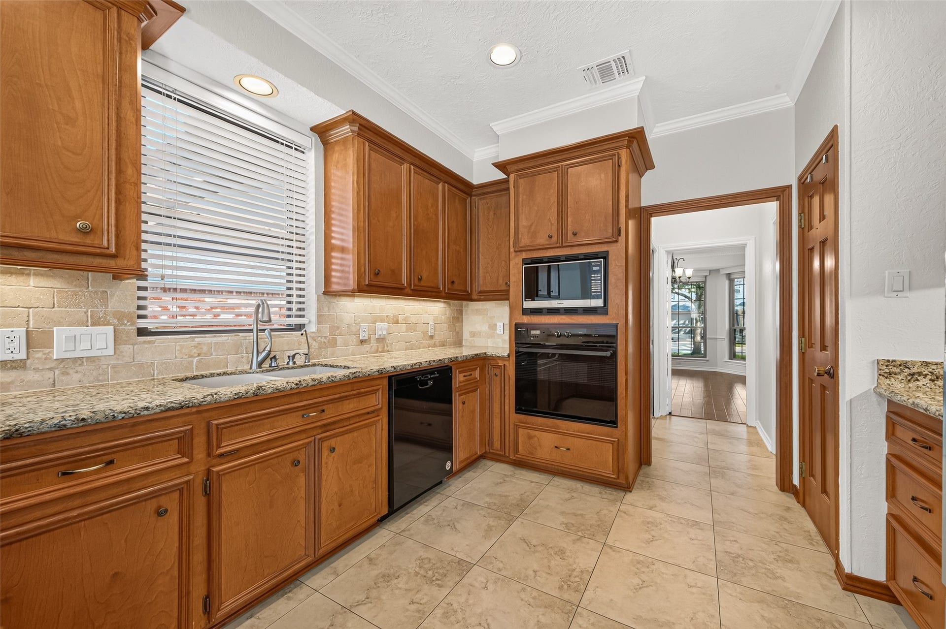 EVERYTHING HAS ITS PLACE! Another view of the kitchen highlights the built-in Jenn-Air oven & Panasonic microwave, conveniently positioned together for meal preparation. The nearby spacious, lighted walk-in pantry provides welcome storage for groceries, small appliances & those extra ingredients you like to keep on hand. Between the kitchen & formal dining is the utility room that offers a convenient exterior door to the porte cochere. Imagine unloading groceries on a rainy afternoon without getting soaked!