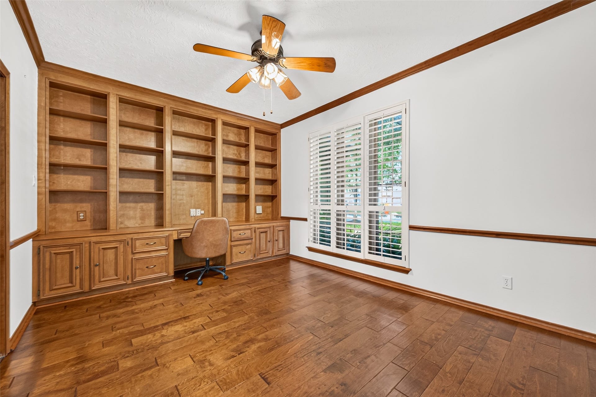WORK FROM HOME IN COMFORT! This inviting first-floor study offers a dedicated workspace with a built-in desk & bookshelves for organizing office essentials, displaying favorite books or showcasing treasured keepsakes. Windows with plantation shutters overlook the front yard, bringing in natural light. Crown molding & a ceiling fan add traditional charm. Whether you envision a home office, cozy library, music room, homeschool classroom or hobby space, this versatile room offers wonderful possibilities!