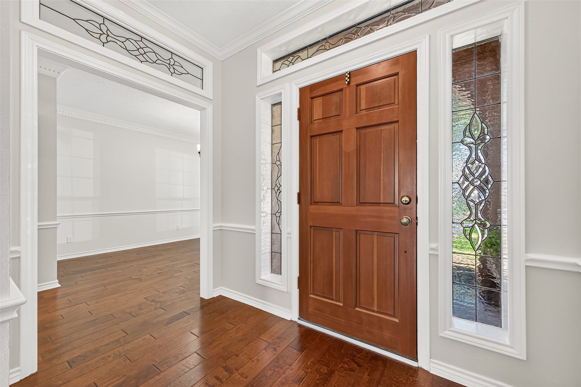 STEP INSIDE & FEEL RIGHT AT HOME! The inviting foyer introduces you to the beautiful architectural details found throughout this classic home. Rich hardwood floors, elegant crown molding & decorative leaded-glass sidelights framing the front door create a warm first impression. Notice the coordinating leaded-glass transom windows above the doorways, adding another touch of character. Just beyond the foyer, the formal dining room awaits, ready for everything from holiday celebrations to intimate dinners.