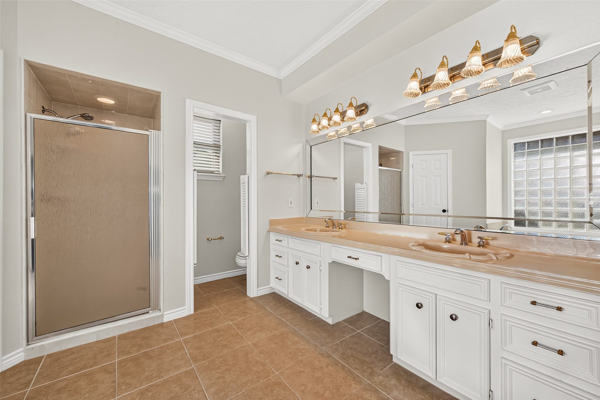 ROOM FOR EVERYTHING & EVERYONE! This view of the primary bathroom showcases the long double vanity with two sinks, generous countertop space & plenty of built-in drawers and cabinets to keep everyday essentials organized. Notice the convenient knee space between the sinksperfect for a vanity stool when getting ready in the morning! The separate walk-in shower features tiled walls & ceiling, a frosted glass door & recessed lighting. A private water closet adds to the practicality of this well-planned bath.