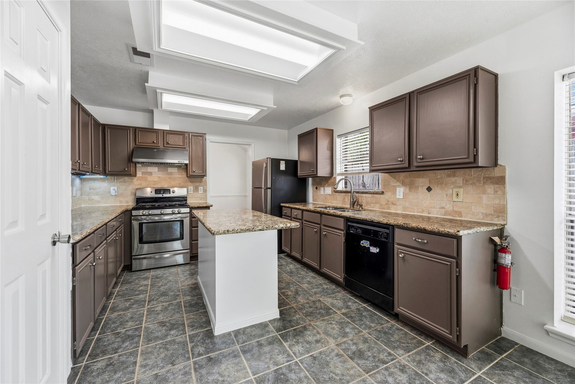 Large kitchen island, granite countertops, and  a stainless steel gas range + vent hood.