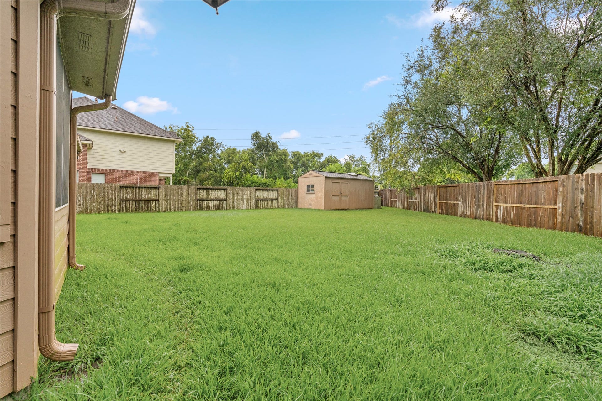 Large fenced backyard framed by mature trees, offering privacy and plenty of room for outdoor activities. The property also includes a substantial storage/work shed, giving buyers valuable additional space for projects, equipment, hobbies, and organization.