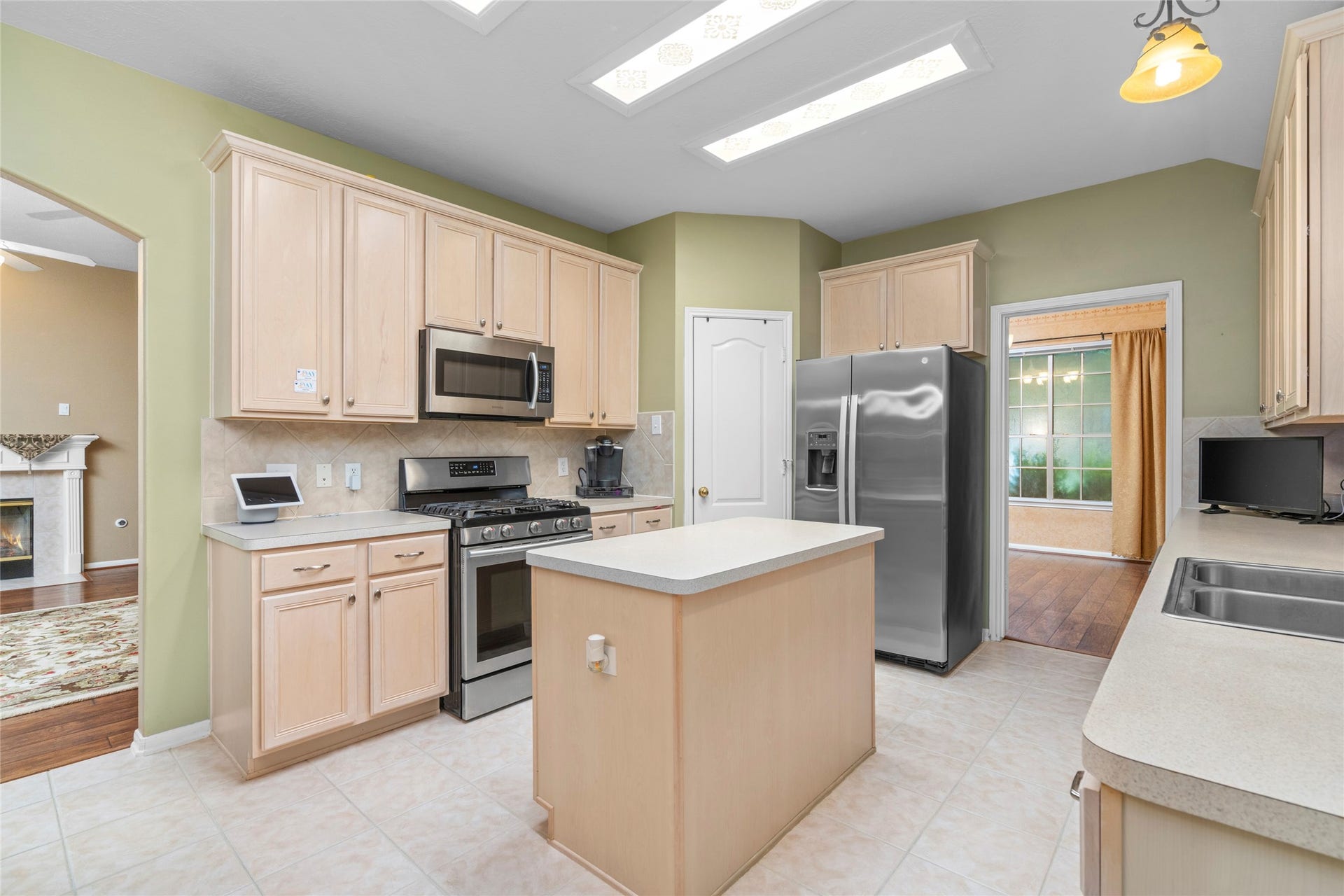 Bright kitchen with an island and plentiful cabinetry, enhanced by natural light from overhead skylights. The generous workspace and open feel give buyers flexibility to personalize the kitchen while retaining the functionality of the existing layout.