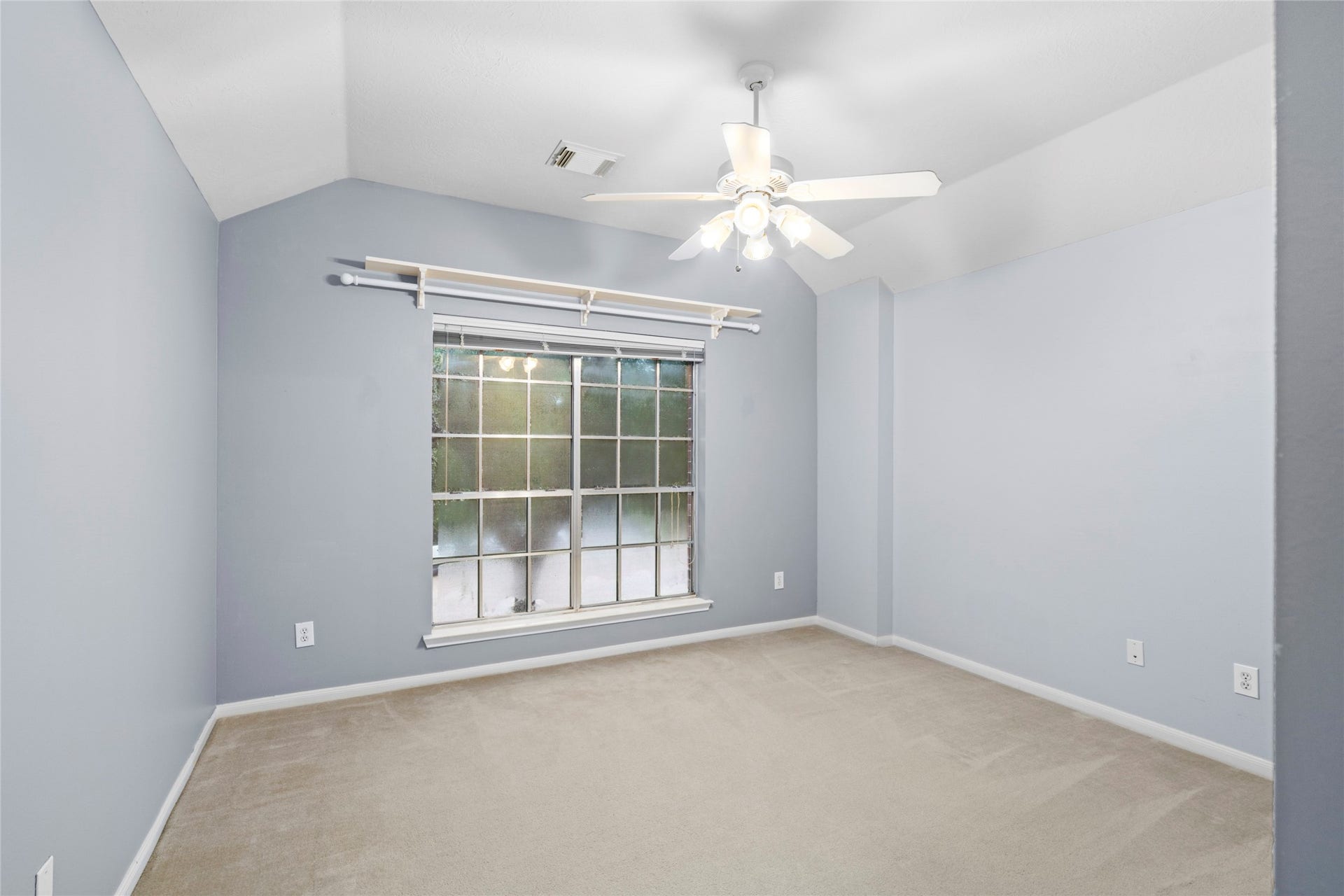 Bright bedroom with soft blue walls, carpeting, ceiling fan, and a large window for natural light. The room offers a calm foundation that a buyer can easily personalize to match their style.