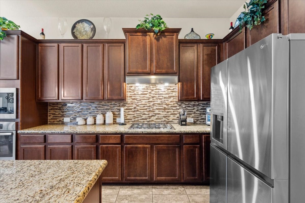 4329 S Meridian Greens Drive, Dickinson, TX 77539 Rich wood cabinetry, tile backsplash, and stainless steel refrigerator.