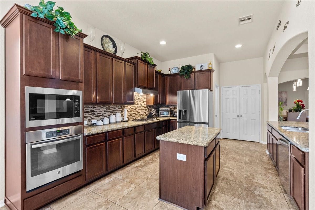 4329 S Meridian Greens Drive, Dickinson, TX 77539 Kitchen with rich wood cabinetry, granite counters, stainless appliances, and a center island.