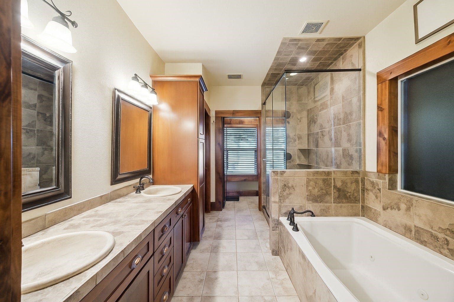 Stone tile surrounds the oversized jetted tub and walk-in shower in this luxurious ensuite bathroom. Dual vanities and generous cabinetry provide both elegance and function in a space designed for everyday pampering.
