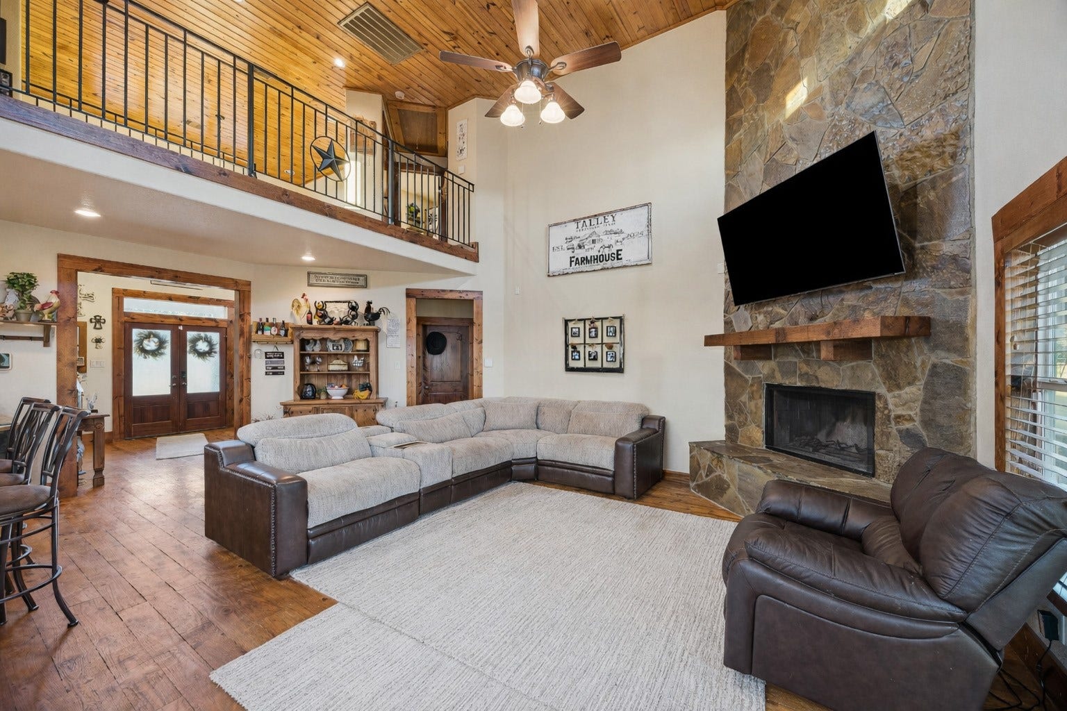 This view from the main entry captures the full scale and flow of the open-concept living room, loft, and entryway. Accents of wood and iron railings, vaulted ceilings, and glowing natural light all combine to showcase the craftsmanship throughout.