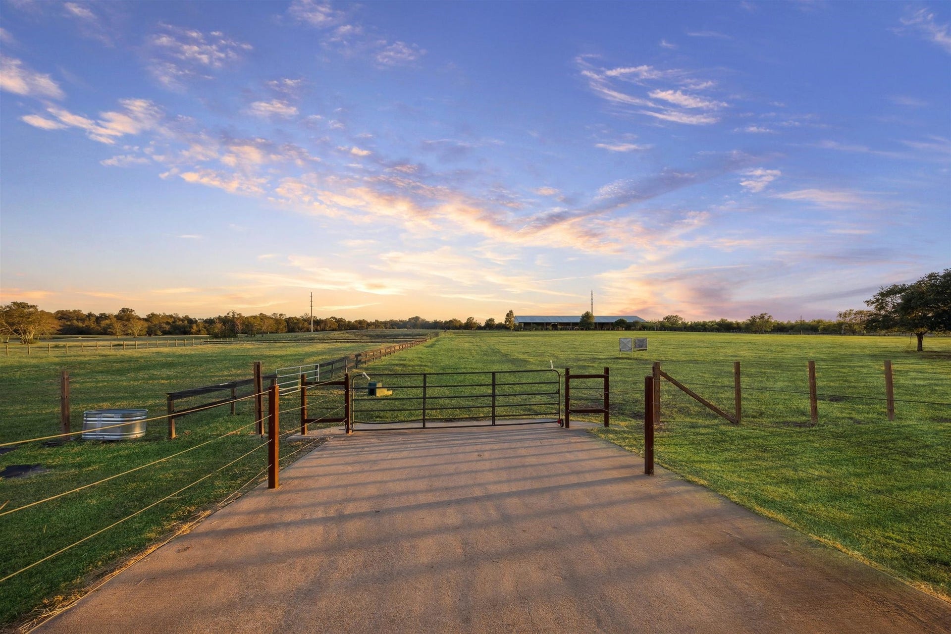 A secure entry leads out into the main pasture, with metal fencing and cross fencing visible on both sides. Bathed in golden light, the open field stretches far into the distance an ideal setup for horses, livestock, or peaceful countryside strolls.
