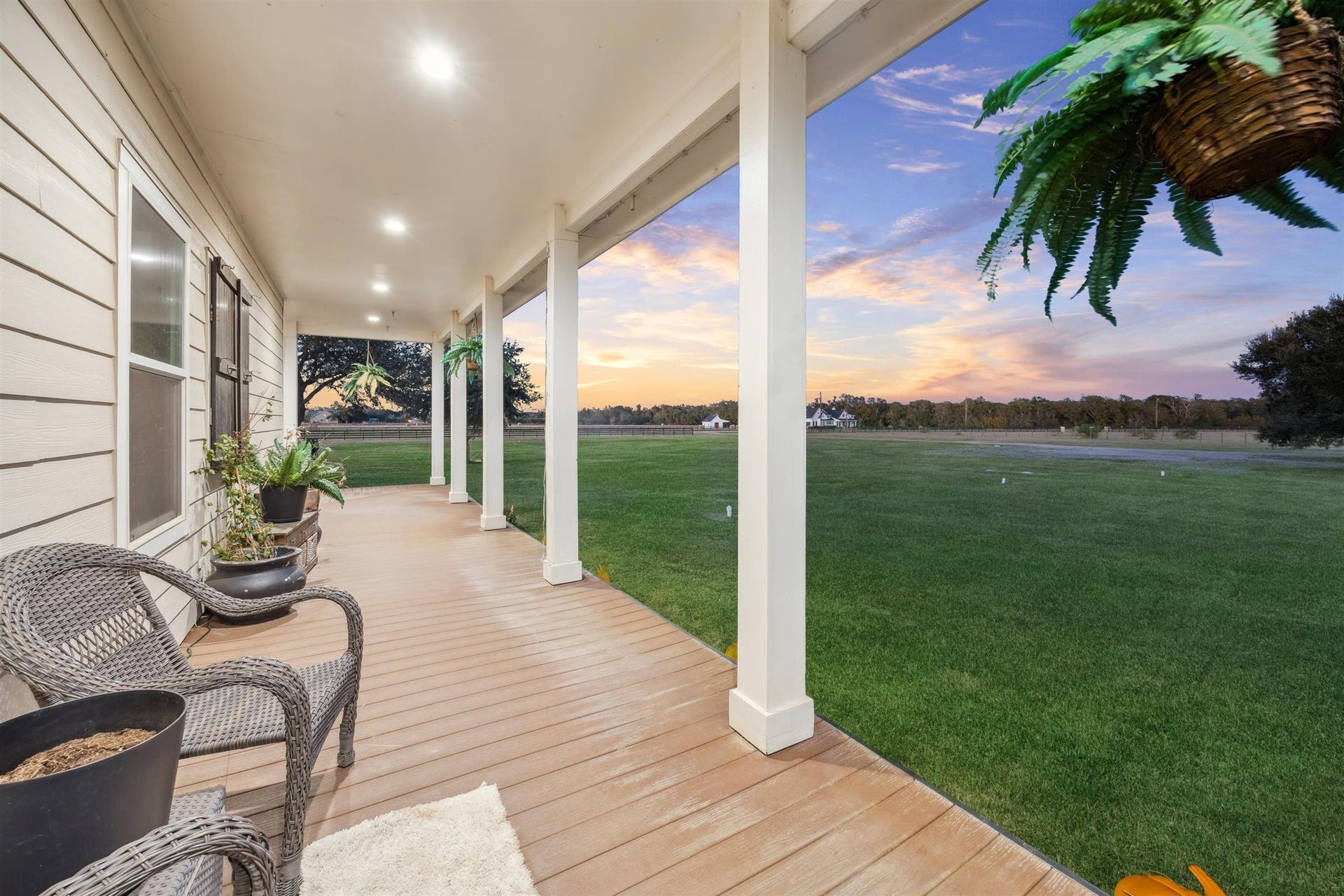 A peaceful escape, this long side porch offers a shaded walkway lined with wicker chairs, potted ferns, and serene country views. With recessed lighting above and an open lawn stretching out beyond, its a perfect place to greet the sunrise or say goodnight to the day on land. The property is a wildlife exemption, adding both beauty and value to the land.
