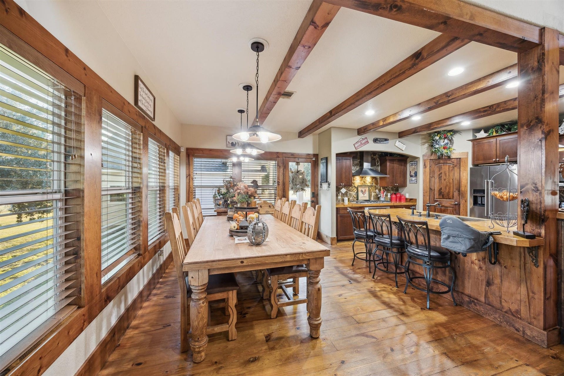 This spacious dining room is perfect for entertaining, with natural light pouring through walls of windows. The open-concept flow connects effortlessly to the gourmet kitchen and breakfast bar, all framed by rich wood beams and Texas country charm.