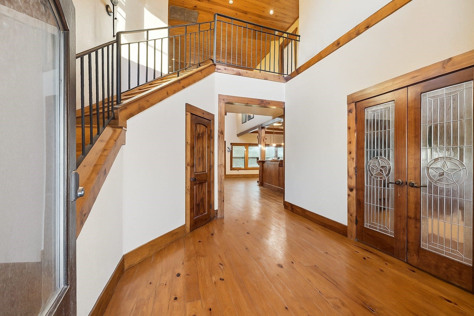 Step into a warm, wood-accented foyer with soaring ceilings, rustic railings, and detailed woodwork. Double glass doors with star-inlay design open into a home filled with Texas character, welcoming guests into a lifestyle of relaxed sophistication. Virtually decluttered to help visualize potential use.