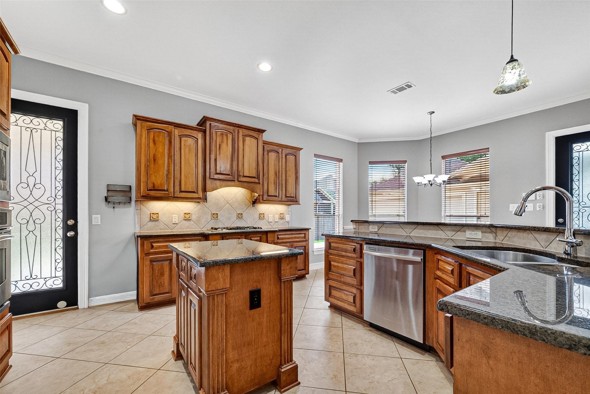3102 Purple Finch, Missouri City, TX 77459 This inviting kitchen features large windows for natural light, a stylish chandelier, and a decorative glass door leading outside. The space is enhanced by neutral tile flooring and a wooden dining set, creating a warm, functional atmosphere.