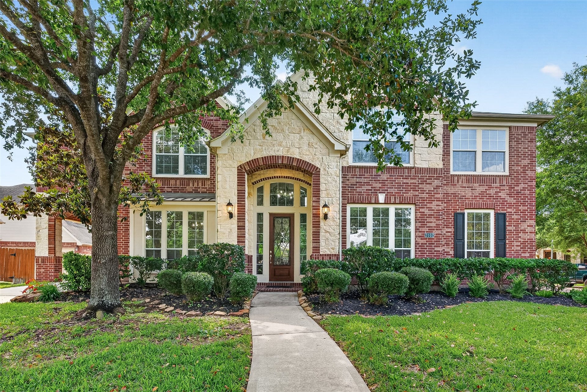 3102 Purple Finch, Missouri City, TX 77459 This 6-bed home is a two-story adorned with brick and stone with a welcoming front facade and lush landscaping. It features a spacious covered driveway leading to a garage, complemented by mature trees and a well-maintained lawn.