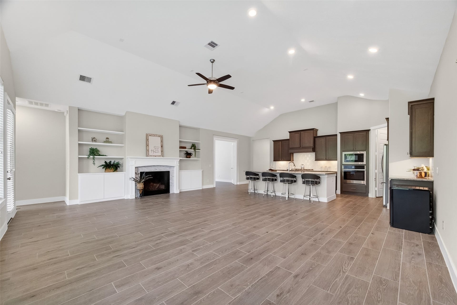 3415 Mckinney Ridge Drive, Houston, TX 77059 This photo showcases the spacious open-concept living area with vaulted ceiling, a cozy fireplace, built-in shelves, and wood-look tile flooring.