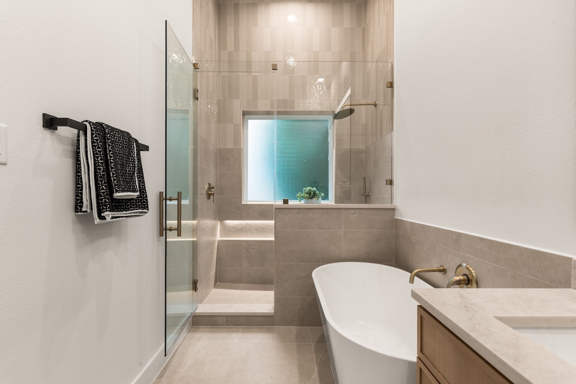 6619 Avenue Q, #A/B, Houston, TX 77011 Modern primary shower space featuring floor-to-ceiling tilework, niche storage, and warm brass fixtures.