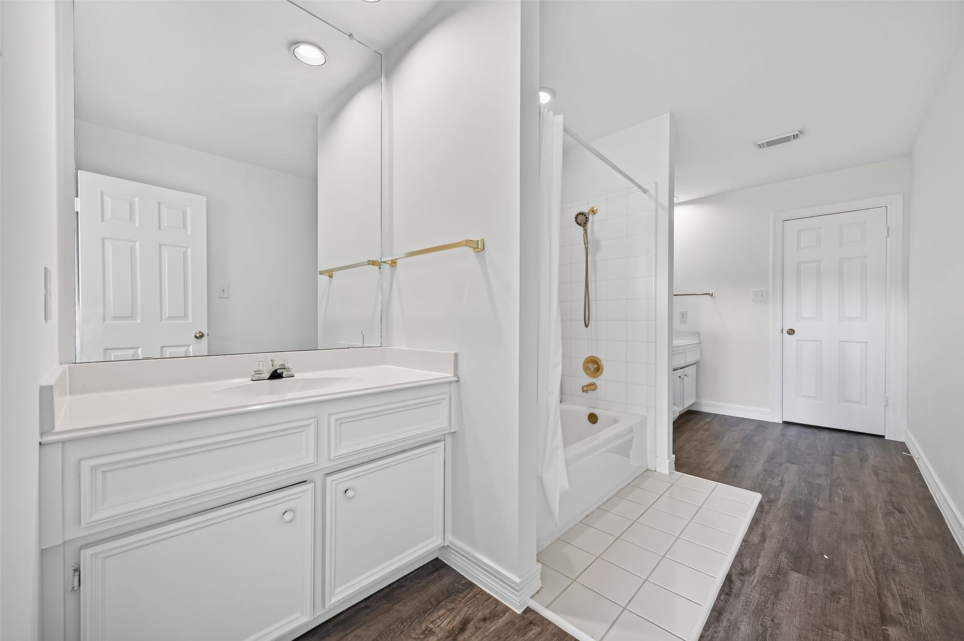 18 Tredington Street, Sugar Land, TX 77479 Bright and spacious bathroom featuring a large vanity with ample cabinets, a classic white tub with gold fixtures, and elegant dark flooring.