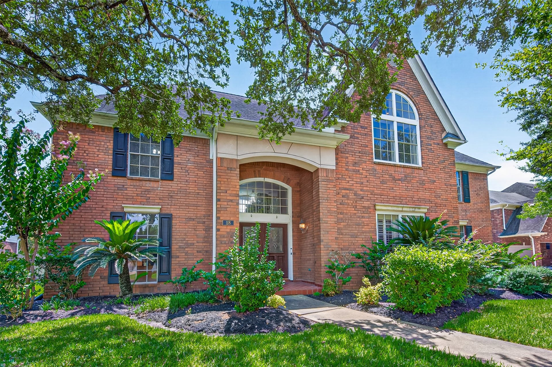 18 Tredington Street, Sugar Land, TX 77479 Stately brick home with elegant arched windows, lush landscaping, and a welcoming entrance framed by mature trees.