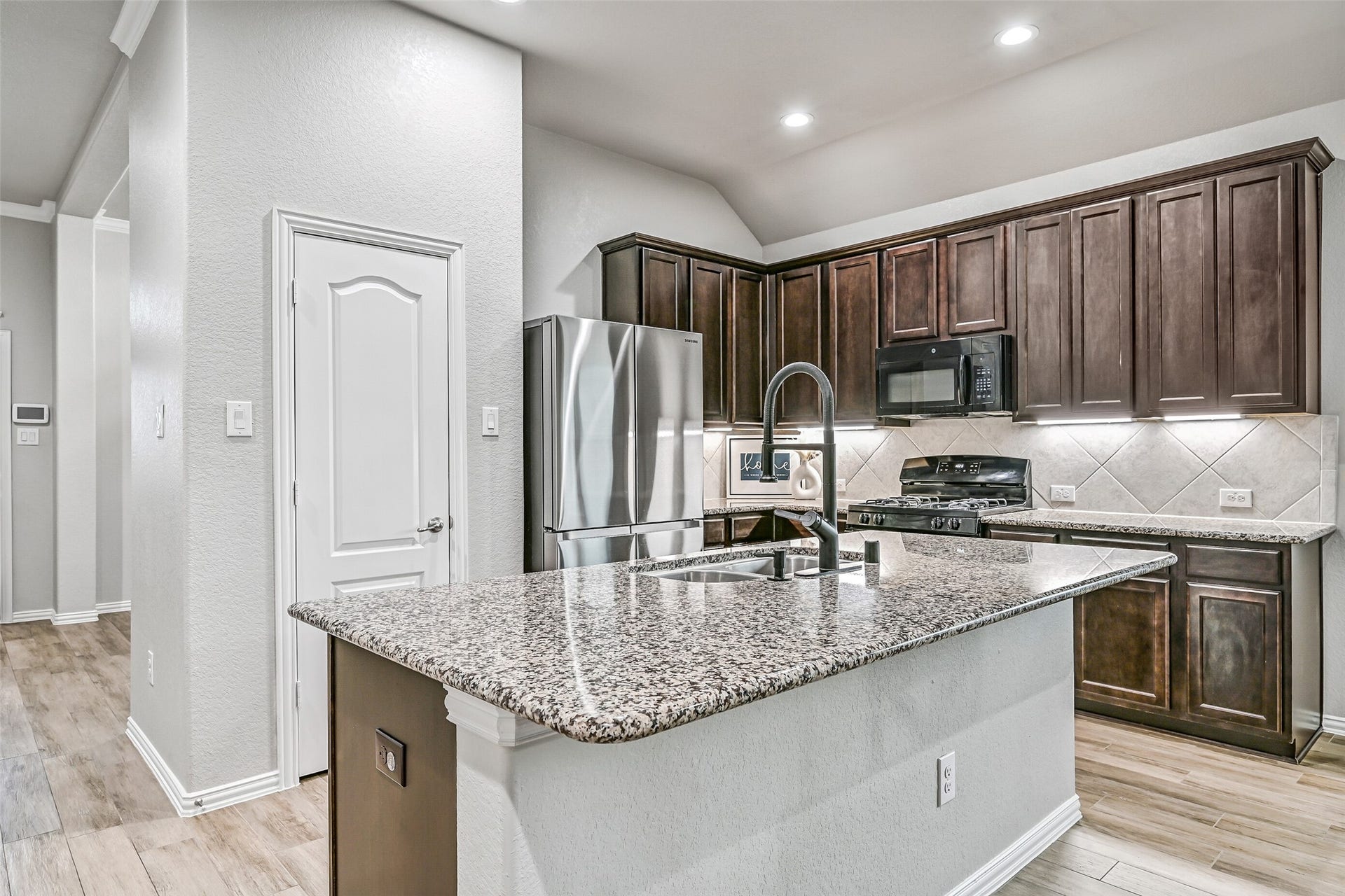 The island kitchen is beautifully appointed with granite countertops, rich 42-inch espresso cabinetry, under-cabinet lighting, stainless appliances, a spacious pantry, and a breakfast bar that's perfect for casual meals or visiting with guests.