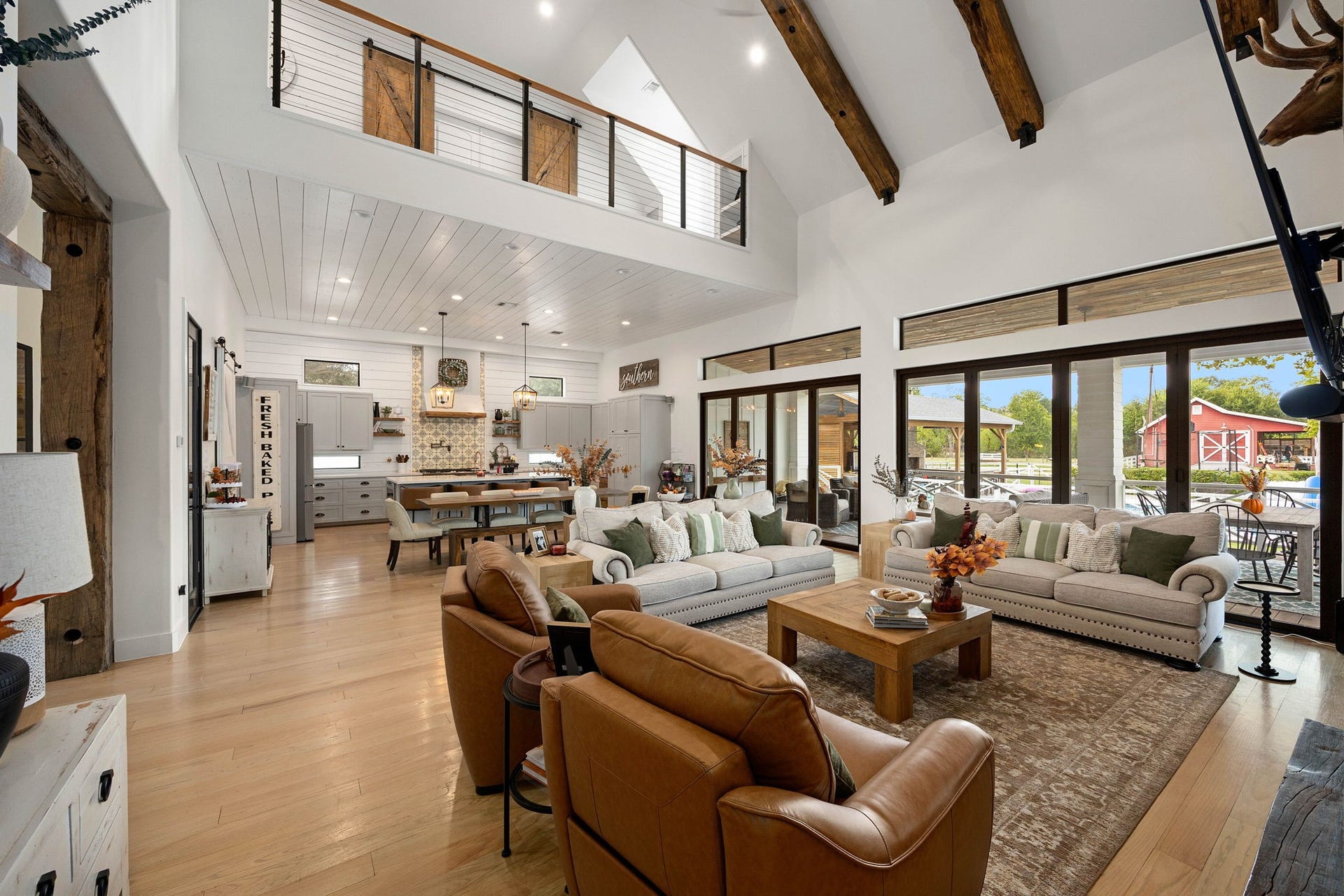 6571 Manorwood Drive, Katy, TX 77493 This panoramic view showcases the masterful flow of the estate, where the dramatic grand living room seamlessly connects to the gourmet kitchen and a second-story loft overlook featuring modern cable railings and custom mini barn doors. The continuous banks of multi-slide glass patio doors frame stunning views of the backyard acreage and outdoor entertainment pavilion.