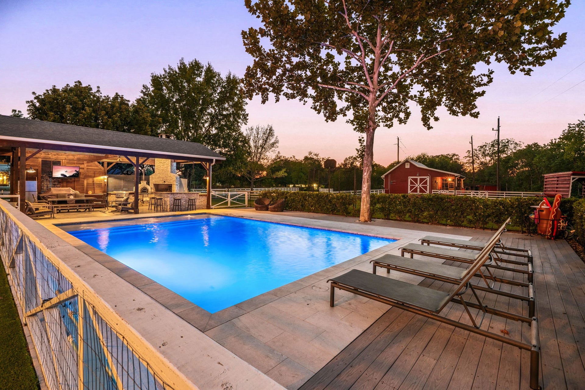 6571 Manorwood Drive, Katy, TX 77493 This expansive angle highlights the seamless flow between the pool deck and the full outdoor kitchen, while capturing the timeless charm of the neighborhood's acreage lifestyle, complete with a classic red barn.