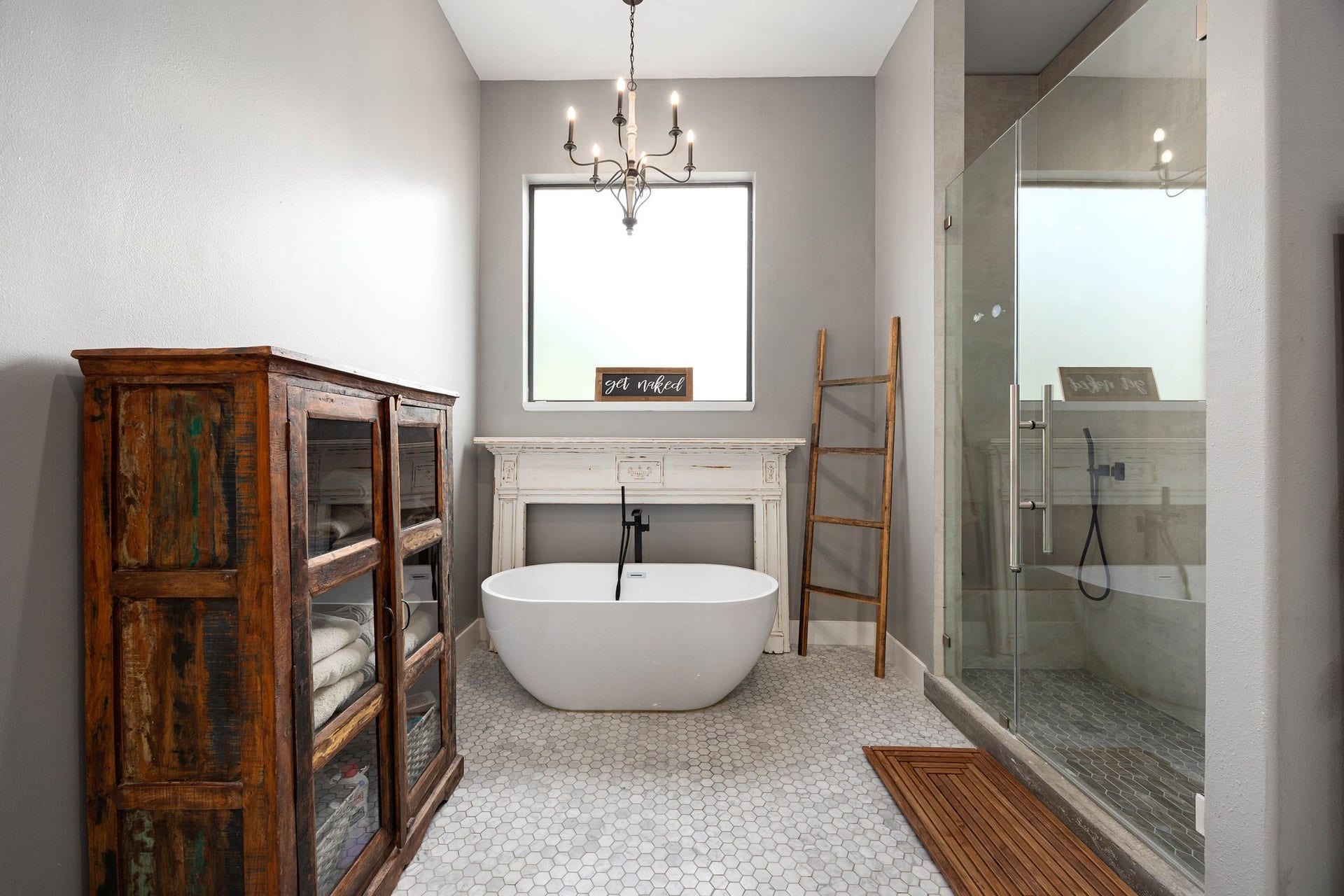 6571 Manorwood Drive, Katy, TX 77493 This beautiful bathing area features a deep freestanding soaking tub set against a unique architectural mantel accent wall beneath a large privacy window and a rustic chic chandelier. The massive walk-in shower stall enclosed by heavy frameless glass is complete with custom wall tile work, a built-in niche, and high-end plumbing fixtures.