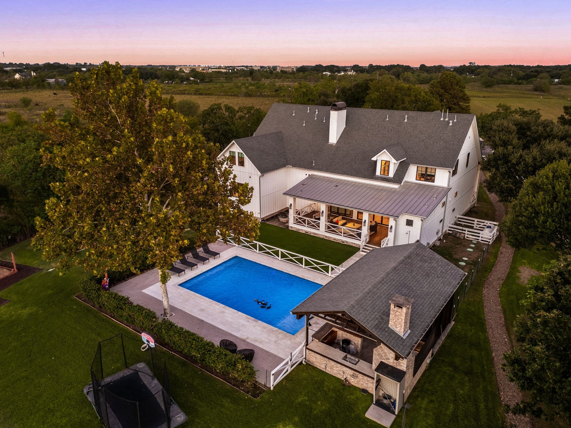 6571 Manorwood Drive, Katy, TX 77493 This aerial shot highlights the seamless layout of the custom farmhouse, glowing heated pool, sprawling travertine deck, and the fully equipped outdoor kitchen pavilion.