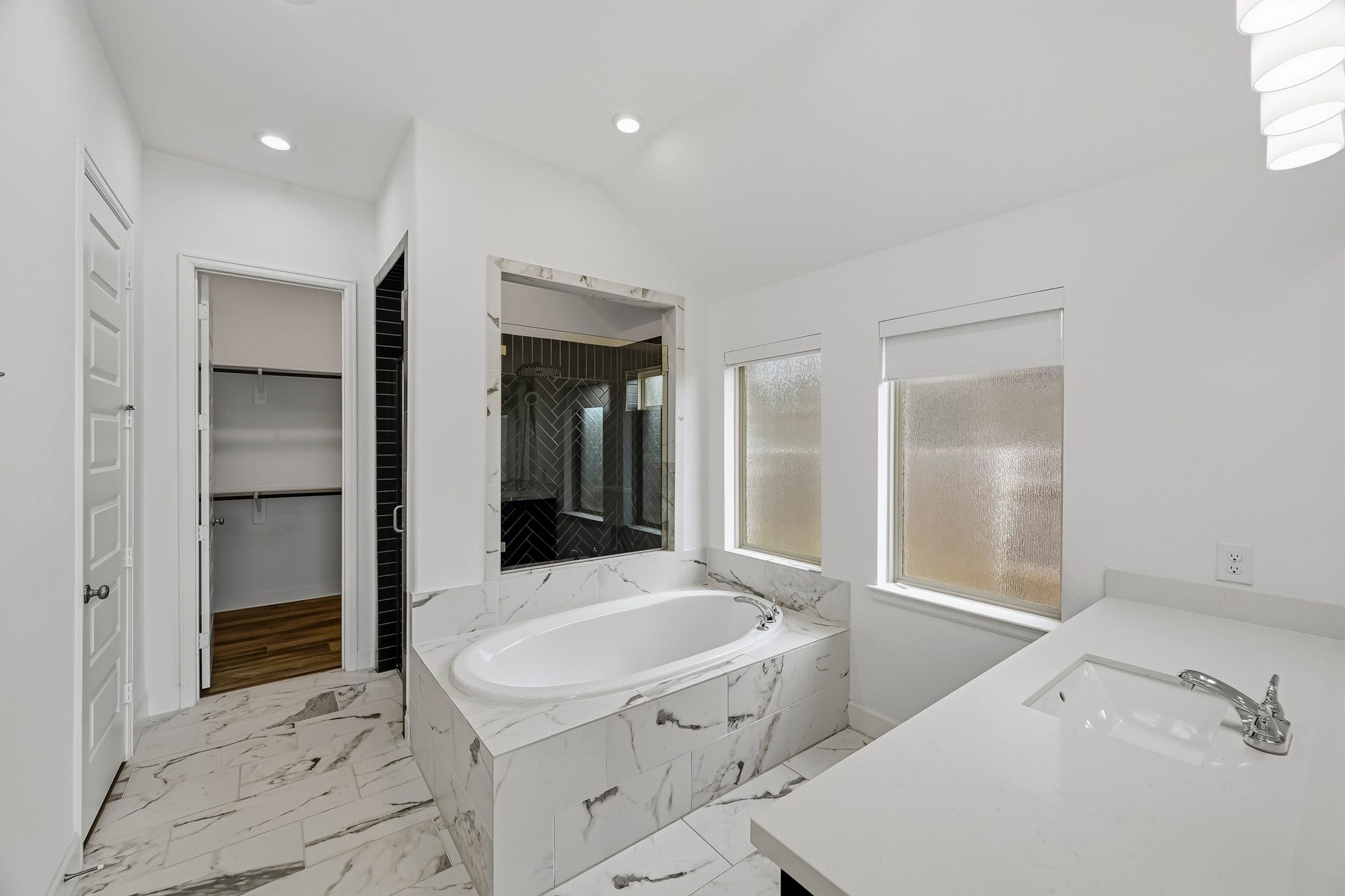 24919 Hibiscus Garden Way, Katy, TX 77493 Welcome to an expansive master bath where vaulted ceilings and recessed lighting create an open, luminous sanctuary. Polished marble-style tile extends beneath a built-in soaking tub, filled with soft natural light from large privacy windows.