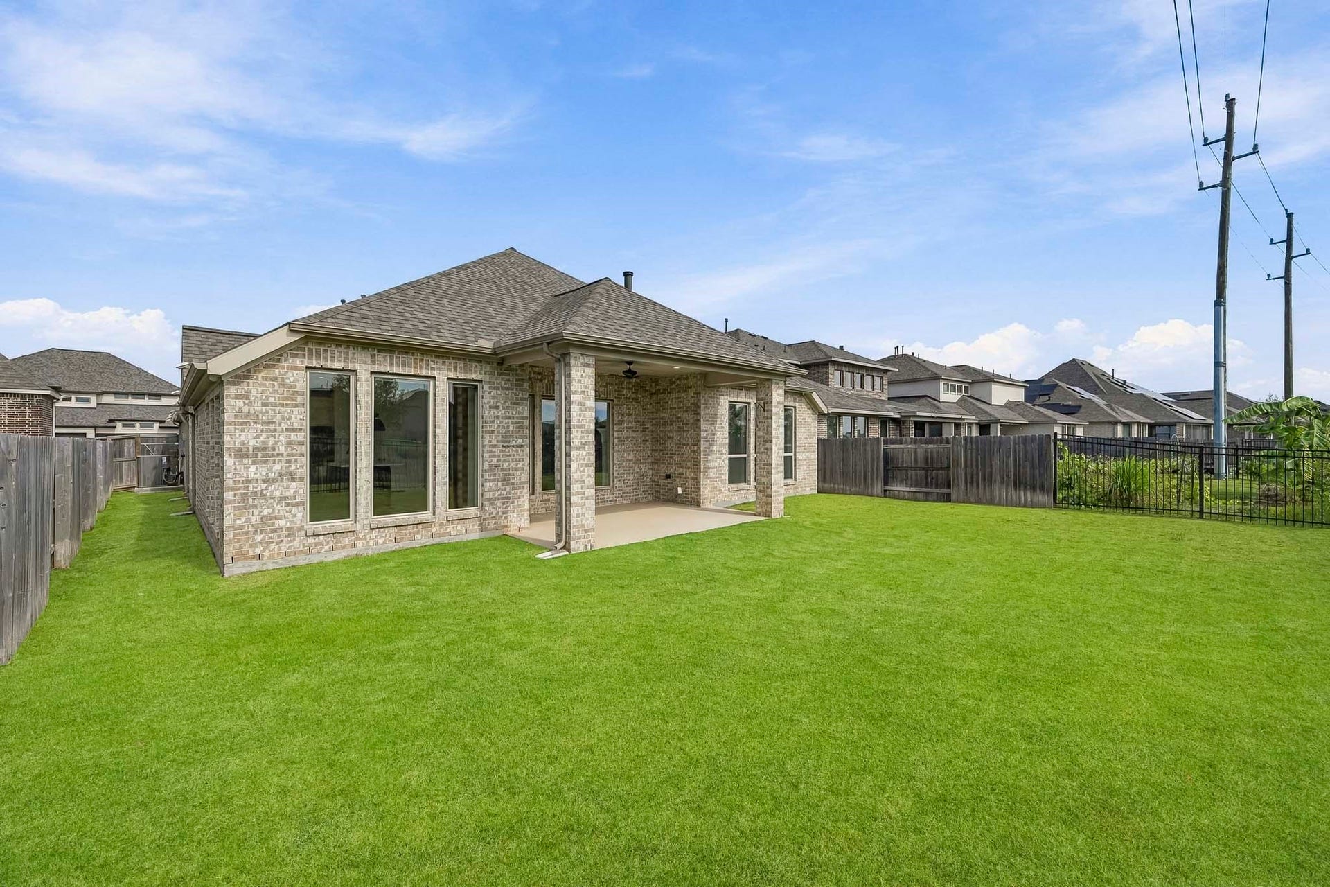 24919 Hibiscus Garden Way, Katy, TX 77493 This property boasts a substantial backyard featuring an expansive, level lawn bordered by perimeter fencing. The exterior design is anchored by an all-brick facade and a generous covered back patio supported by substantial brick columns, offering seamless indoor-outdoor living with views of the vast green space.