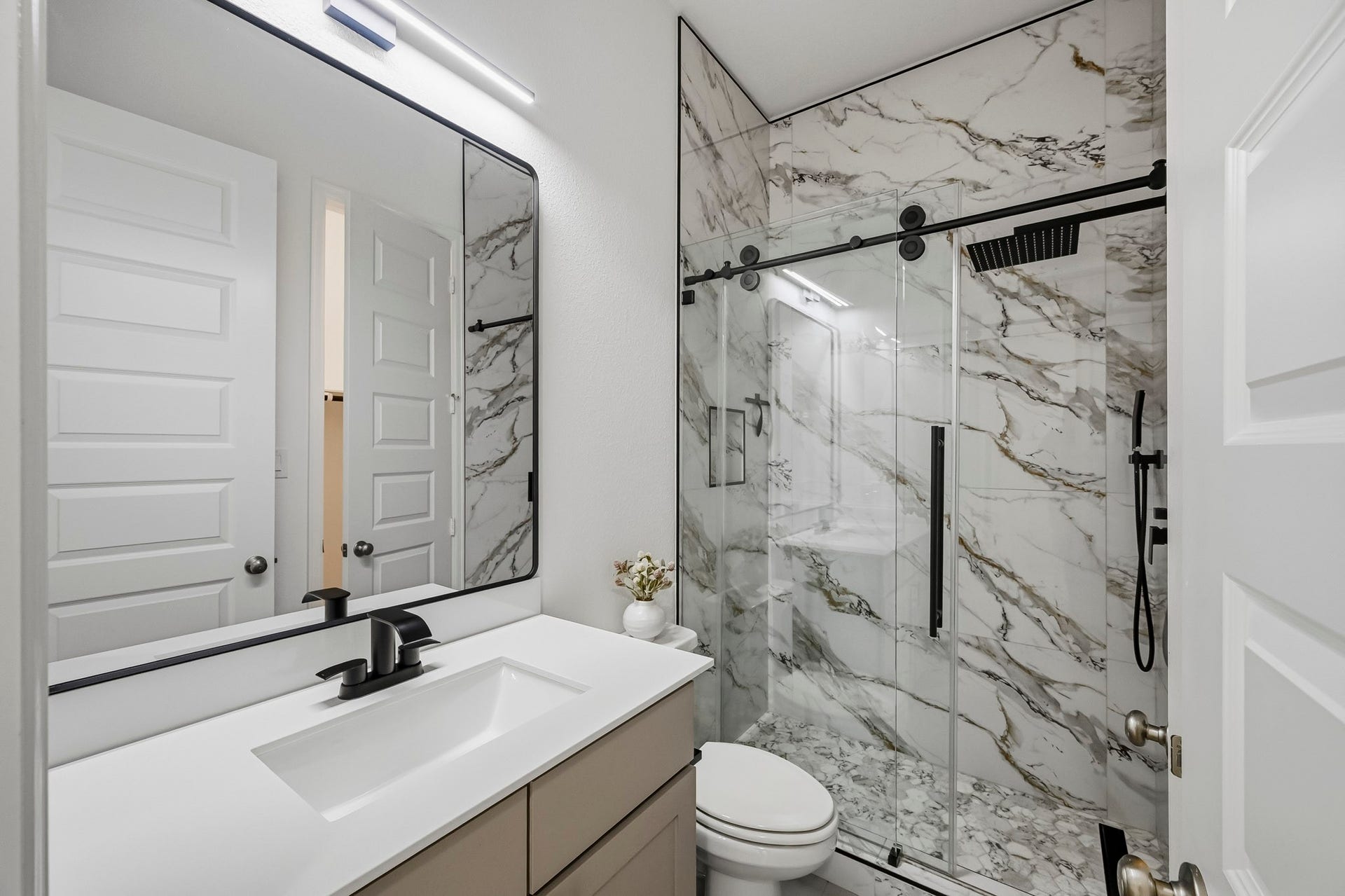 24919 Hibiscus Garden Way, Katy, TX 77493 Sophisticated finishes define this well-proportioned secondary bathroom retreat. Highlights include premium marble-pattern wall surfaces extending through the glass-enclosed shower, streamlined hardware, and an expansive wall mirror.