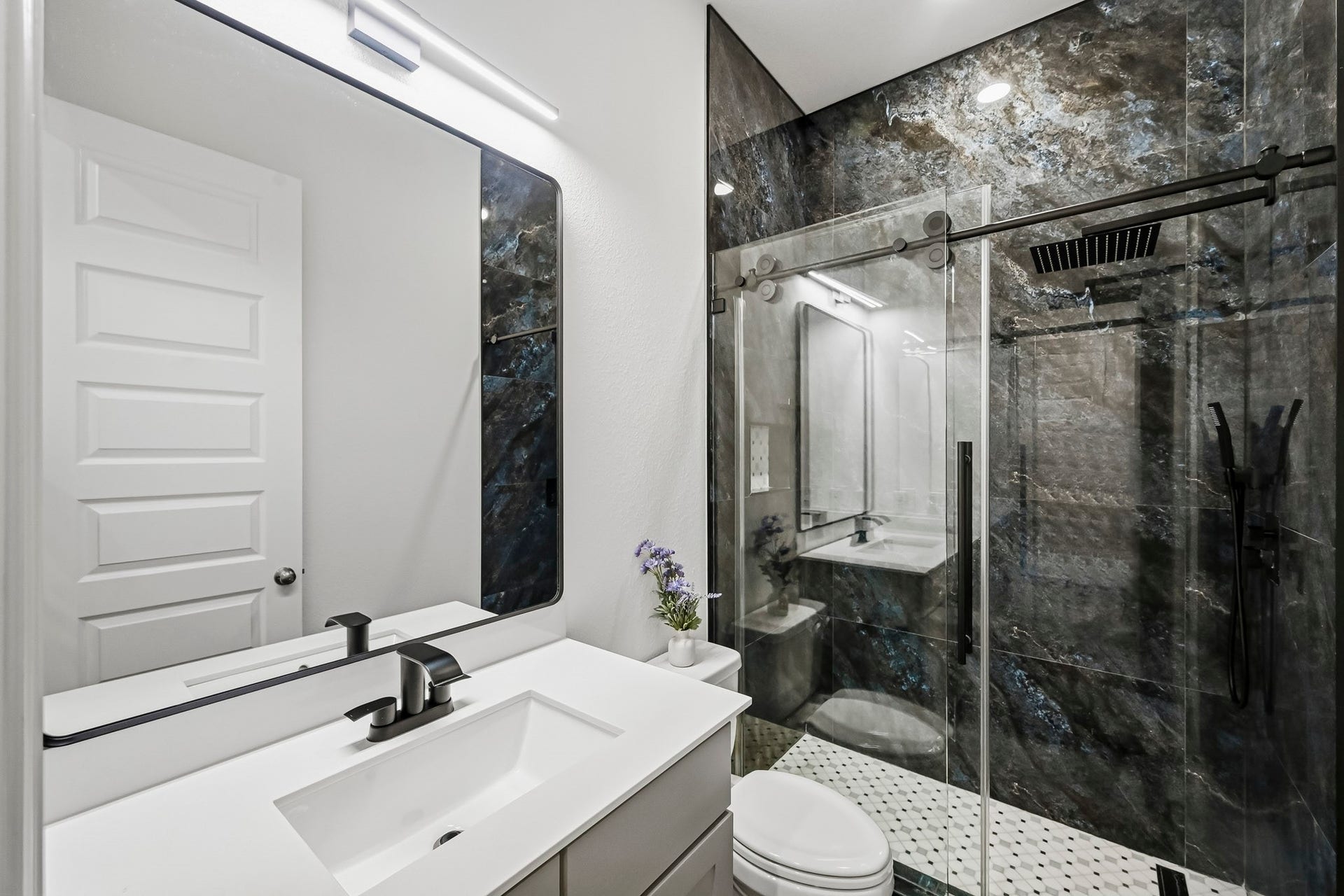24919 Hibiscus Garden Way, Katy, TX 77493 This modern bathroom showcases high-end finishes, highlighted by a spacious walk-in shower enclosed in sliding glass. Striking stone-look wall panels line the shower interior, beautifully paired with geometric tile flooring, an undermount sink basin, and an expansive wall mirror that enhances the room's open feel.