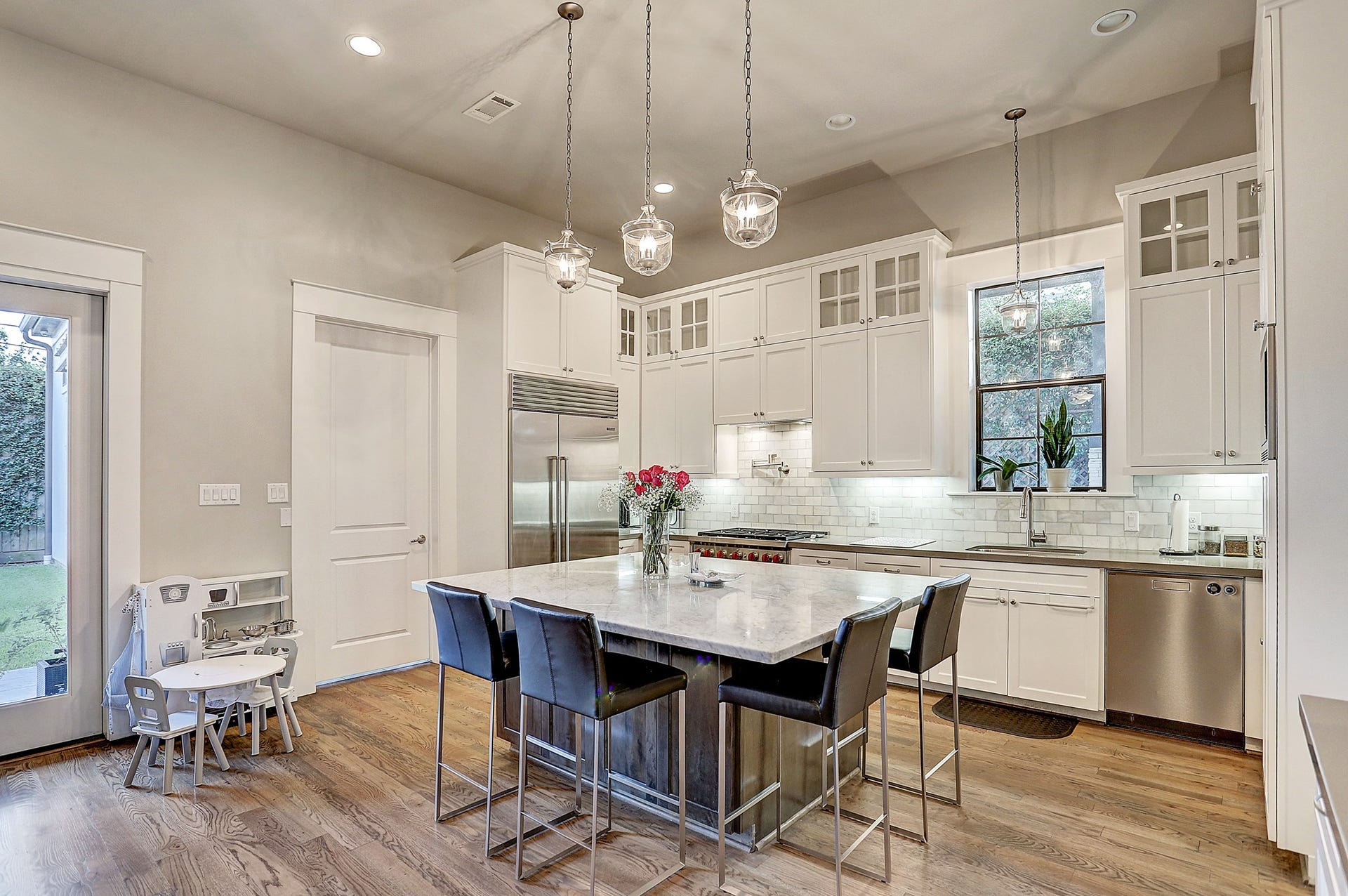 11x16 kitchen has quartz counters along the walls with Carrara marble subway tile backsplash, under-cabinet lighting and stainless steel appliances that includes a 6-burner gas Wolf stove, Wolf microwave, Asko dishwasher, and built-in Sub-Zero refrigerator.