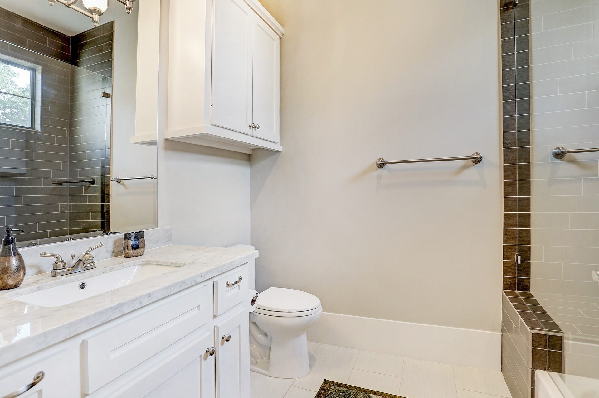 Ensuite bathroom for 2nd bedroom has tile floor, tub/shower combo with seating and subway tile surround, Carrara marble counter, and custom lighting.