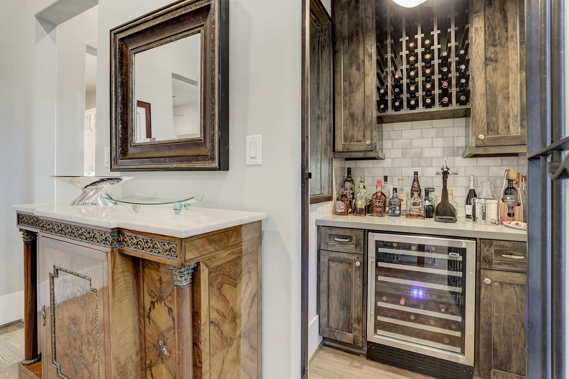 Wine grotto has a dry bar with quartz counter & marble Carrara subway tile backsplash, built in Summit wine refrigerator, wine racks and overhead lighting.
