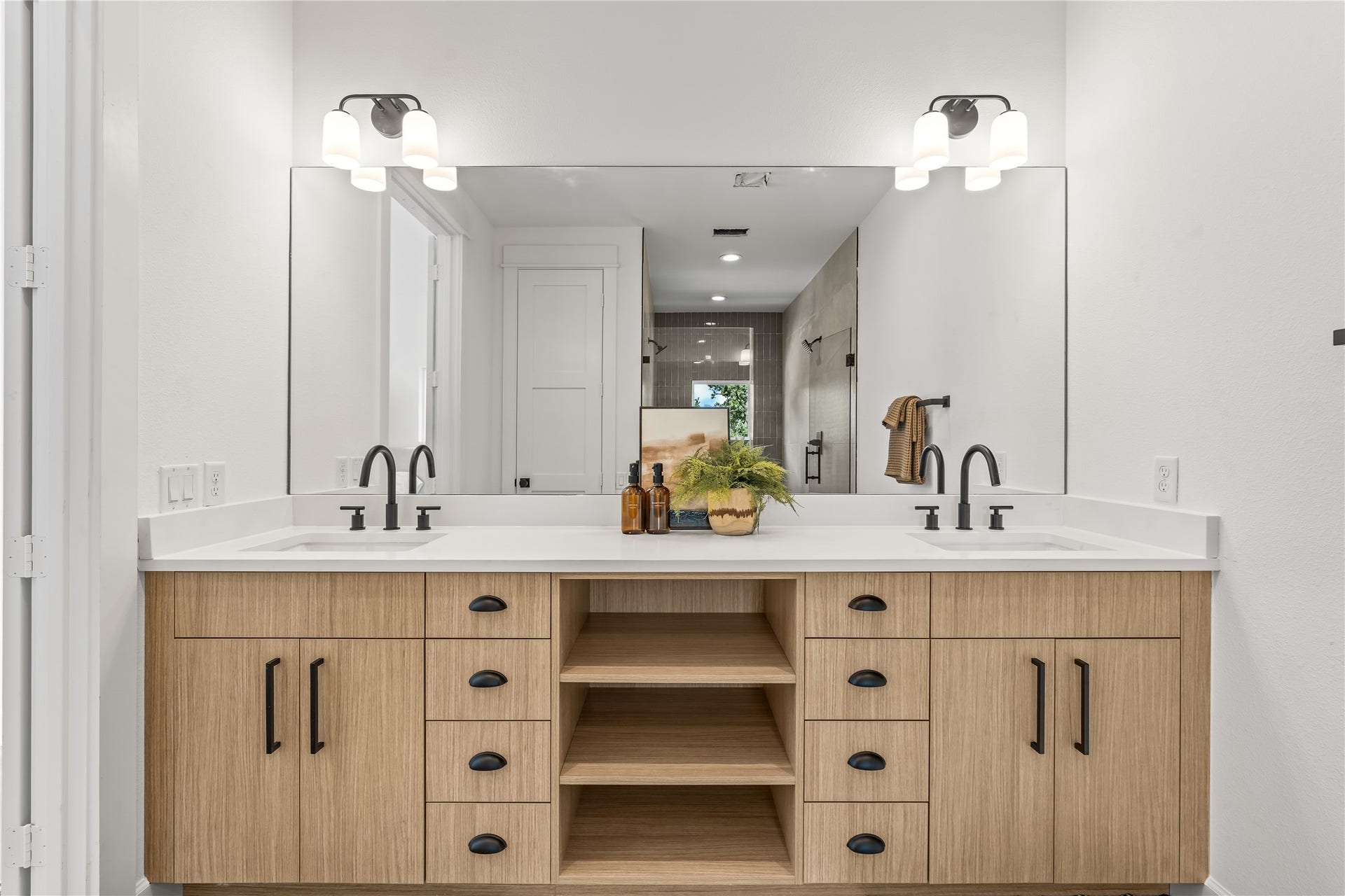7432 & 7444 Tremper Street, Houston, TX 77020 Straight-on view of the primary en-suite bathroom's expansive double vanity with light wood cabinetry, open shelving, and black hardware.
