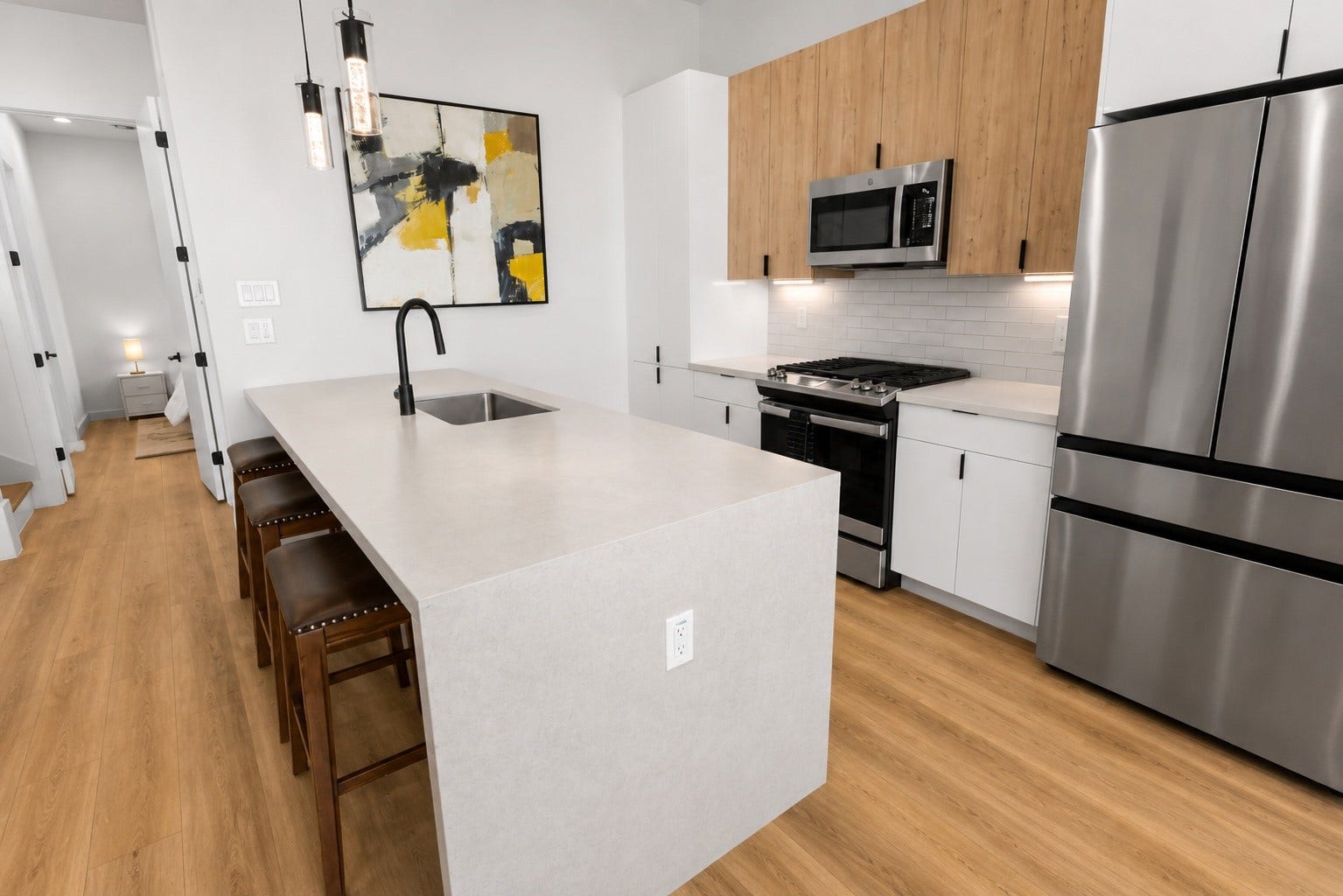 Designed for both entertaining and everyday living, the kitchen centers around an oversized waterfall island with seating, quartz countertops, shaker cabinetry, stainless steel appliances, subway tile backsplash, and under cabinet lighting. Warm wood cabinetry pairs beautifully with crisp white finishes to create a timeless contemporary aesthetic.