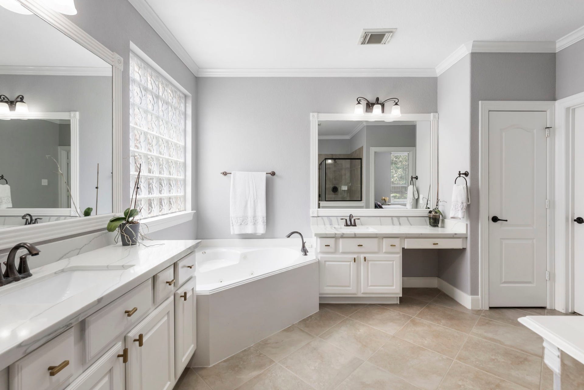 130 S Arrow Canyon Circle, The Woodlands, TX 77389 This spacious bathroom features dual vanities with elegant fixtures, a large soaking tub, and ample natural light from a glass block window. The neutral tones and tile flooring create a modern and inviting atmosphere.
